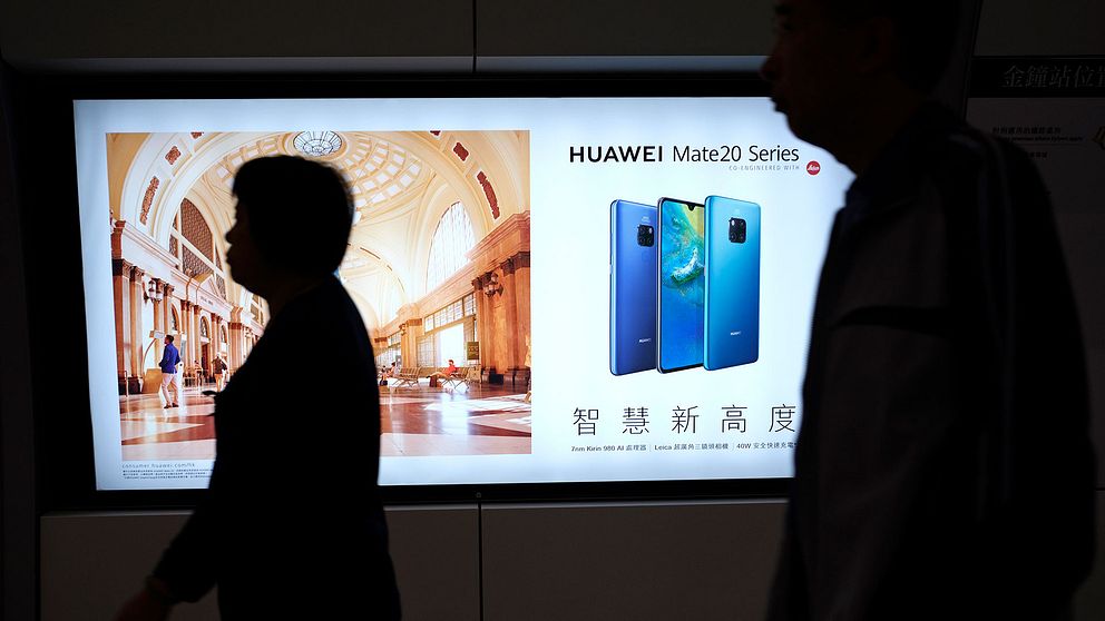 Människor framför reklam för Huawei i Hongkongs tunnelbana