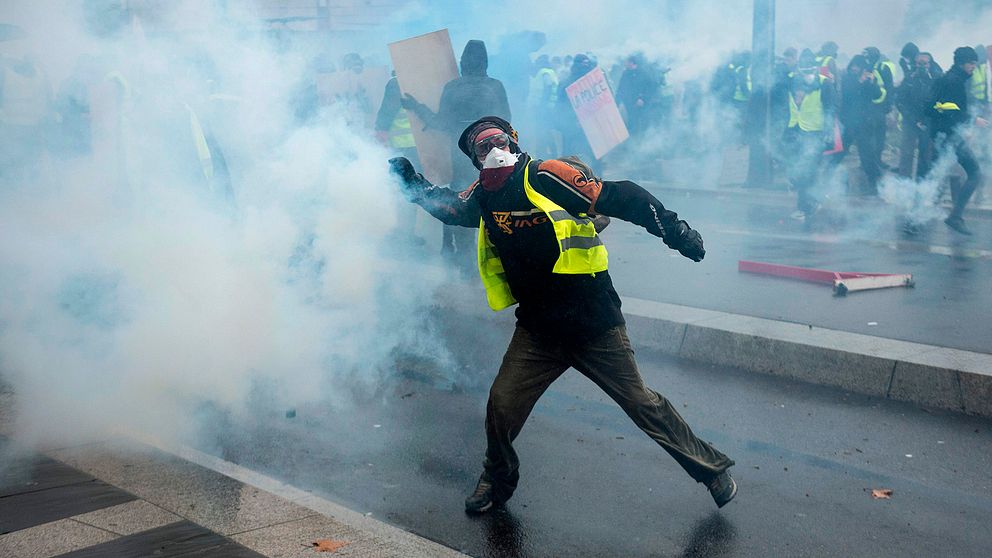 En demonstrant i gul reflexväst kastar tårgas.
