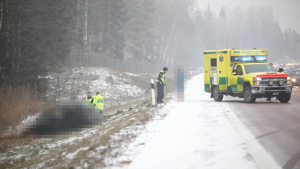 ambulans på vägen, bil i diket, räddningspersonal och en civil person som är blurrad, lite snö på marken