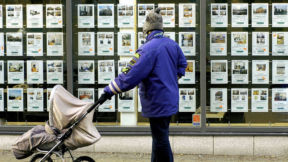 Man med barnvagn tittar på bostadsannonser i skyltfönster.