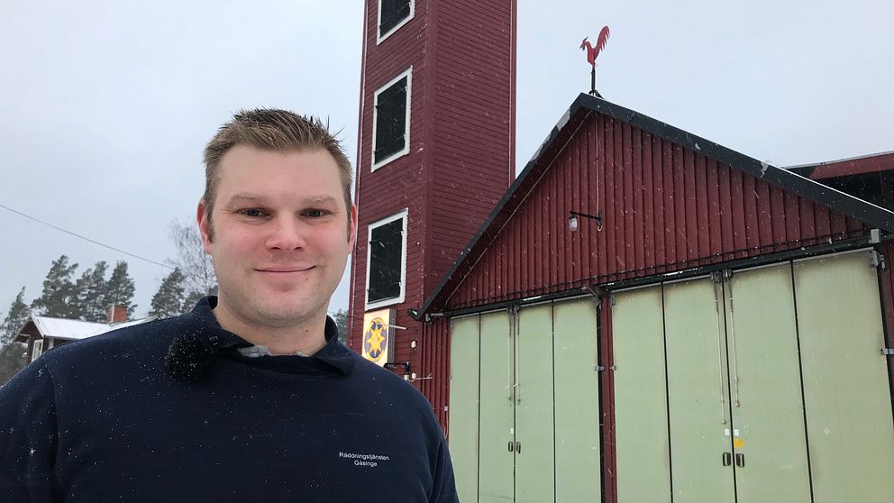 Andreas Andersson framför den röda stationsbyggnaden i byn Avla. Det karaktäristiska tornet och tuppen på taknocken syns i bakgrunden.