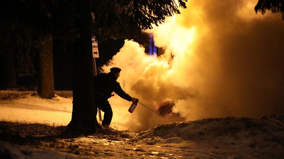 kvällstid vinter, polisman som sprutar med brandsläckare på kraftigt rykande bil
