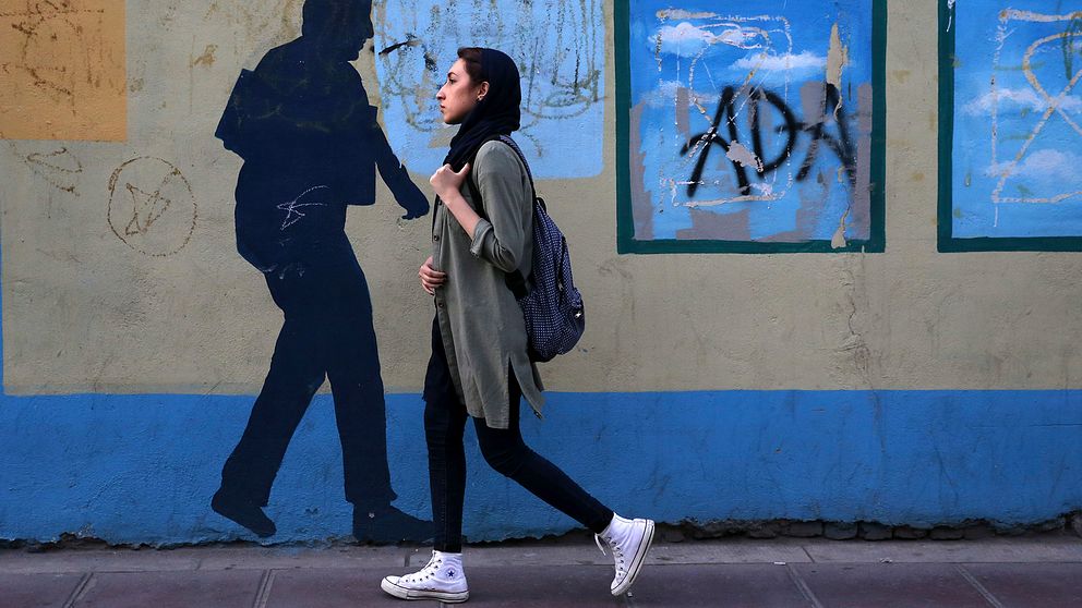 En iransk tjej i Teheran går framför en väggmålning.