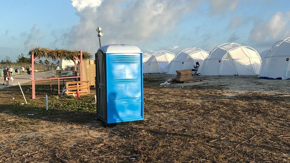Blå bajamaja framför vita tält på en öppen gräsyta under molnig himmel.