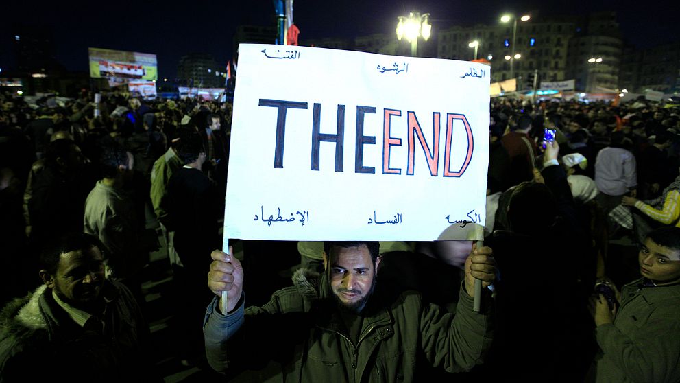 En man håller upp ett plakat där det står: The End