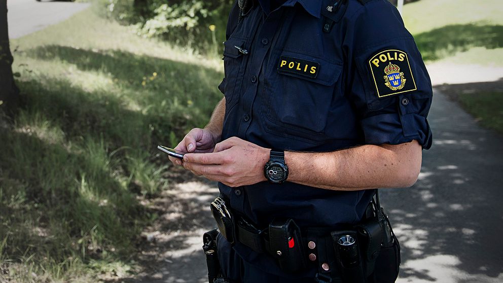 En polis står med en mobiltelefon.