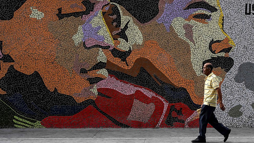 En man går förbi en mosaikvägg föreställande Nicolas Maduro och Hugo Chaves.