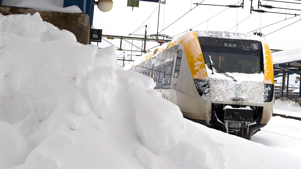 Tåg framför en snöhög på perrongen