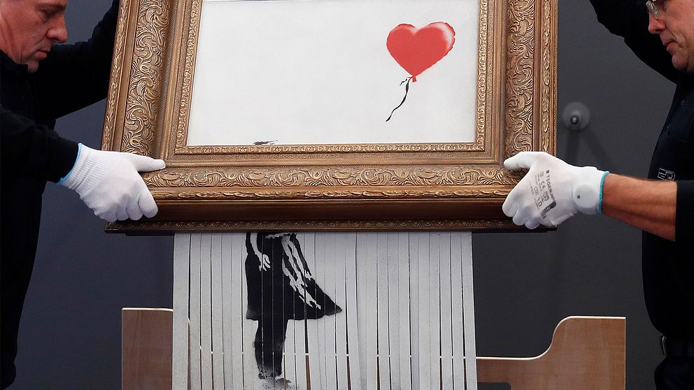 Två män sätter upp Banksys konstverk på en vägg.