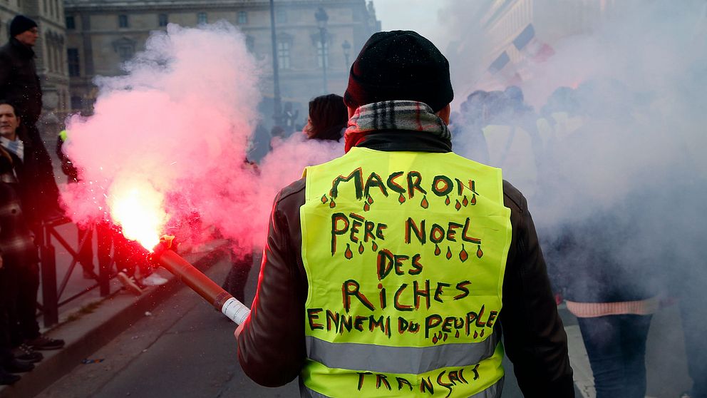 ”Macron, de rikas jultomte, folkets fiende,” står det på demonstrantens rygg.