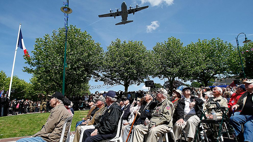 Amerikanska krigsveteraner tittar upp mot ett C130 Air Force-plan som flyger över Sainte-Mere-Eglise i Frankrike under en ceremoni för att hedra fallskärmshoppare.