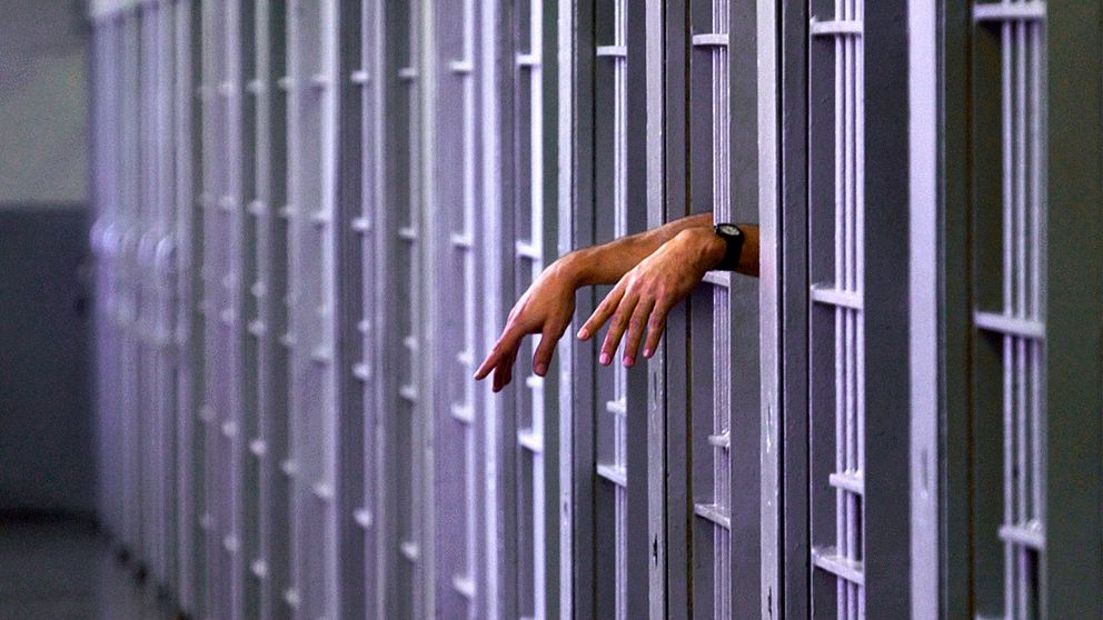 Händer som sticker ut från en fängelsecell.
