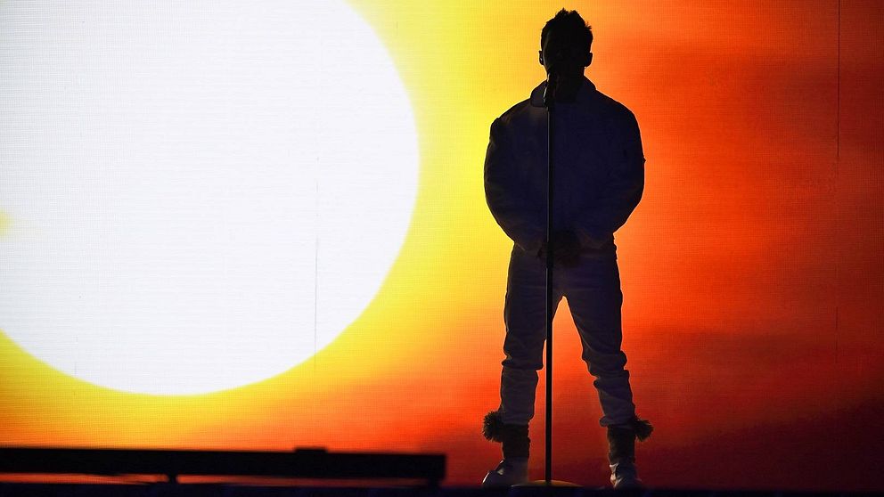 Siluettbild på Jon Henrik Fjällgren framför en stor sol på scenen