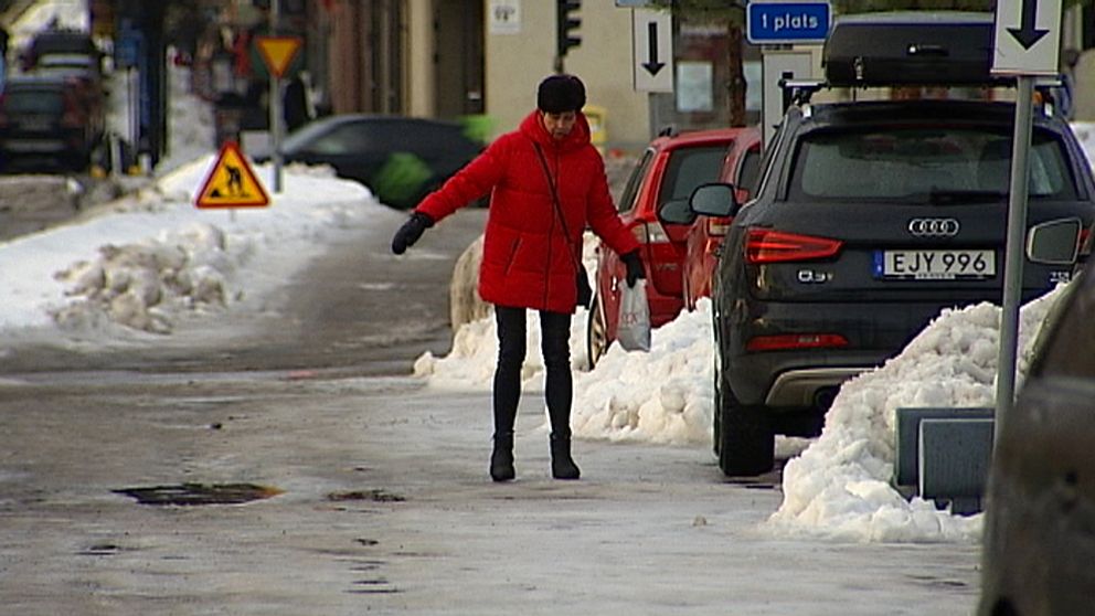 Kvinna i röd jacka som försöker balasera på ishal trottoar.