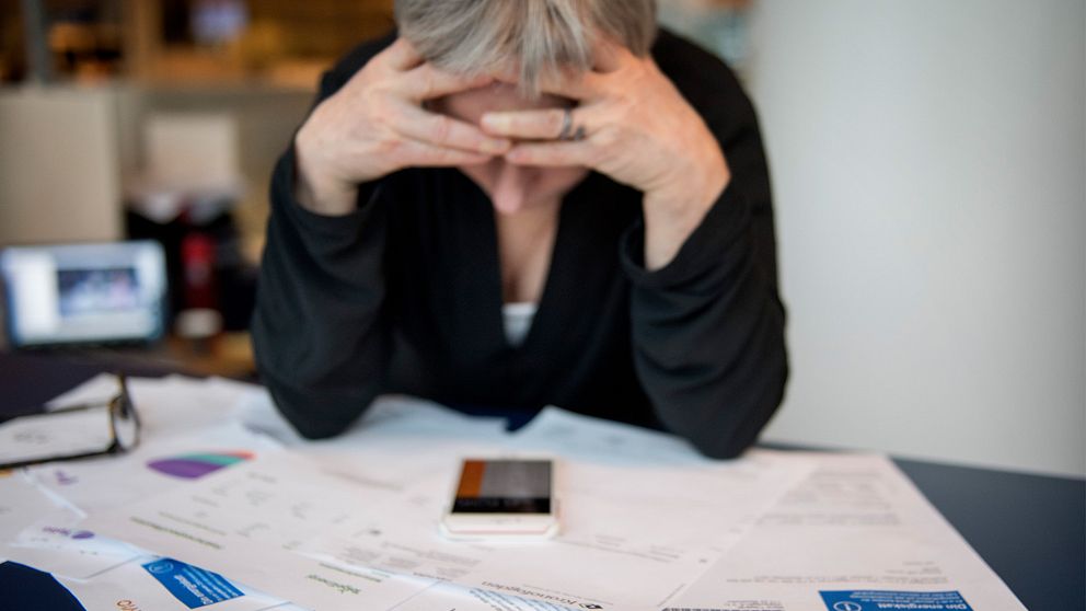 Kvinna som sitter med huvudet i händerna vid ett skrivbord fyllt med räkningar.