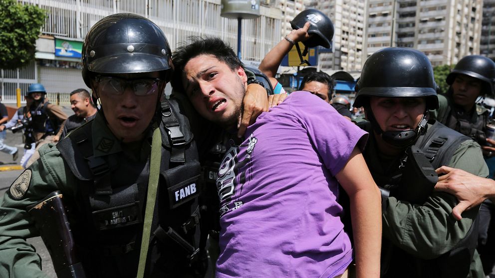 Militärpolis håller venezuelan kring halsen under demonstration.