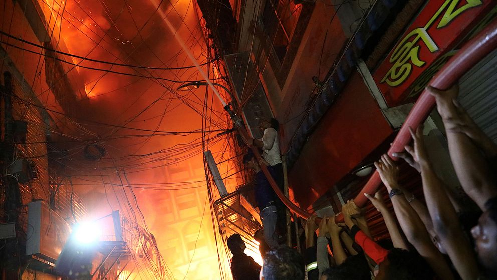 Personer hjälps åt att släcka branden som bröt ut i ett flerfamiljshus som även användes som kemiskt lager i Dhakas äldre delar.