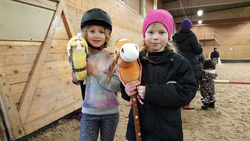 två flickor står med varsin käpphäst