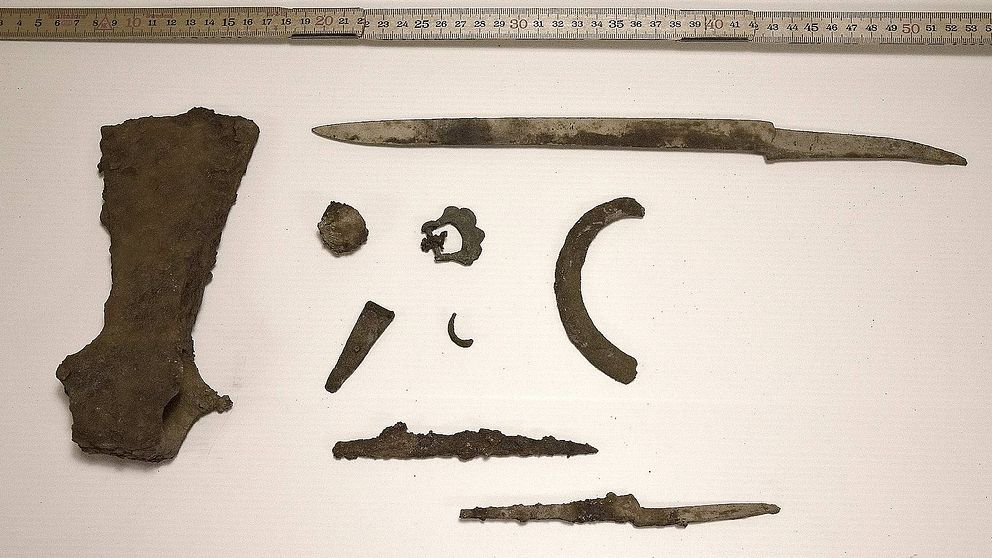 Bild på en rostig yxa, en längre kniv eller svärd och några mindre metallföremål