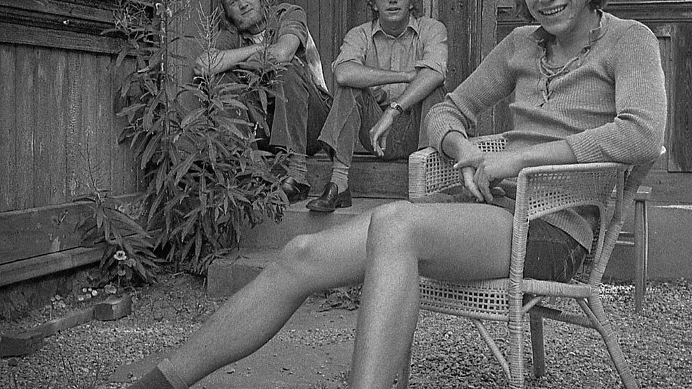 Tre män som sitter framför ett hus – svartvitt foto