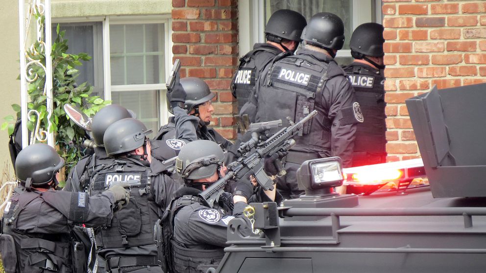 Säkerhetspolis klädda i svart tar sig in genom en dörr i ett hus med vapen höjda.