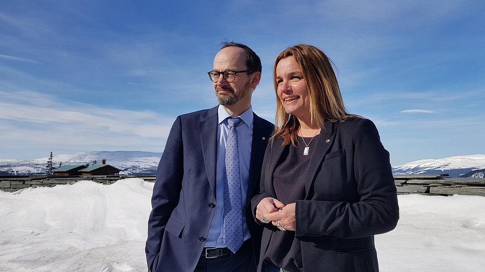 En man (infrastrukturminister Tomas Eneroth) och en kvinna (riksdagsledamoten Anna-Caren Sätherberg) står i solen i Åre och tittar åt vänster.