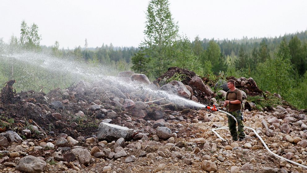 Brandman med vattenslang ute i skogen.