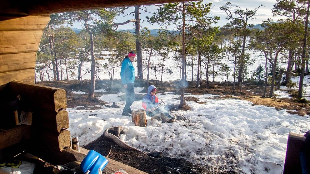 Kvinna och barn grillar korv i snön vid ett vindskydd