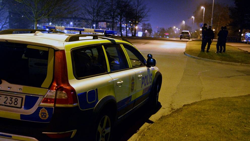 En polisbil i förgrunden och en grupp poliser längre bort, på natten. Bilden är från ett annat tillfälle.