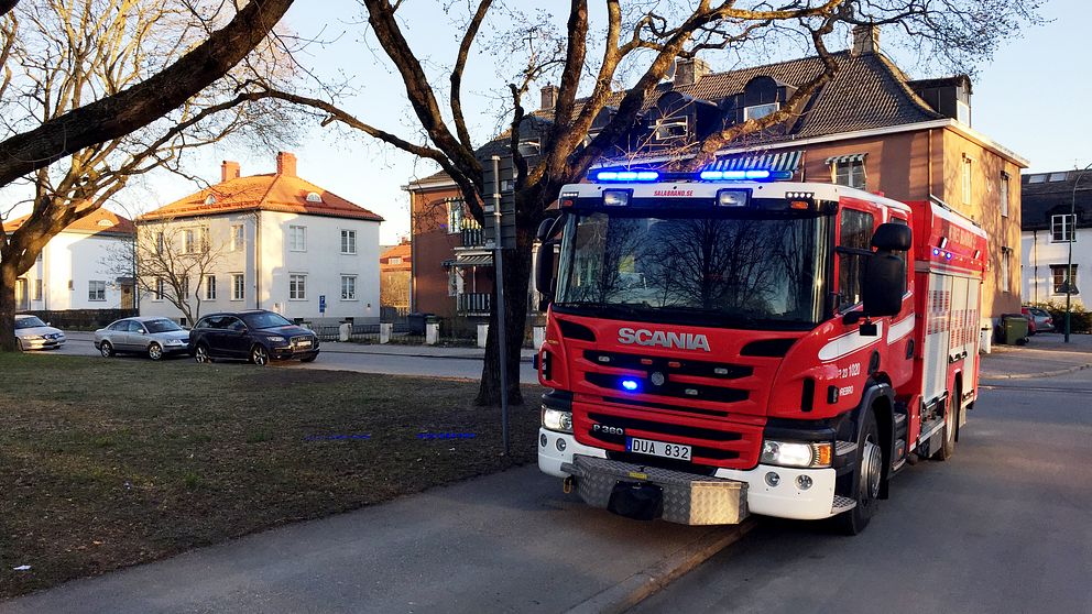 En brandbil från Nerikes brandkår parkerad på trottoaren vid Sveaparken, med ett brunt och ett vitt lägenhetshus i bakgrunden.