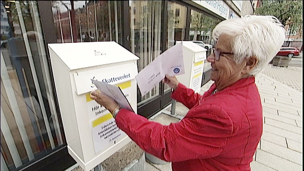 Ingrid Blomen i rödjacka och glasögon lägger ner sin pappersdeklaration i en av Skatteverkets två brevlådor.