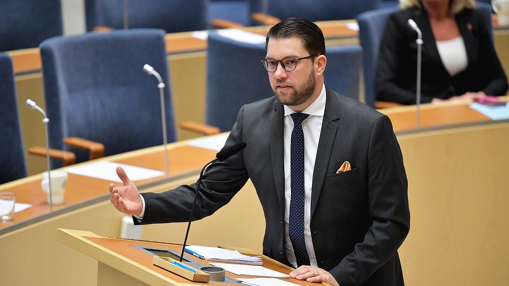 Sverigedemokraternas partiledare Jimmie Åkesson står vid en talarstol och pratar under riksdagsdebatten.