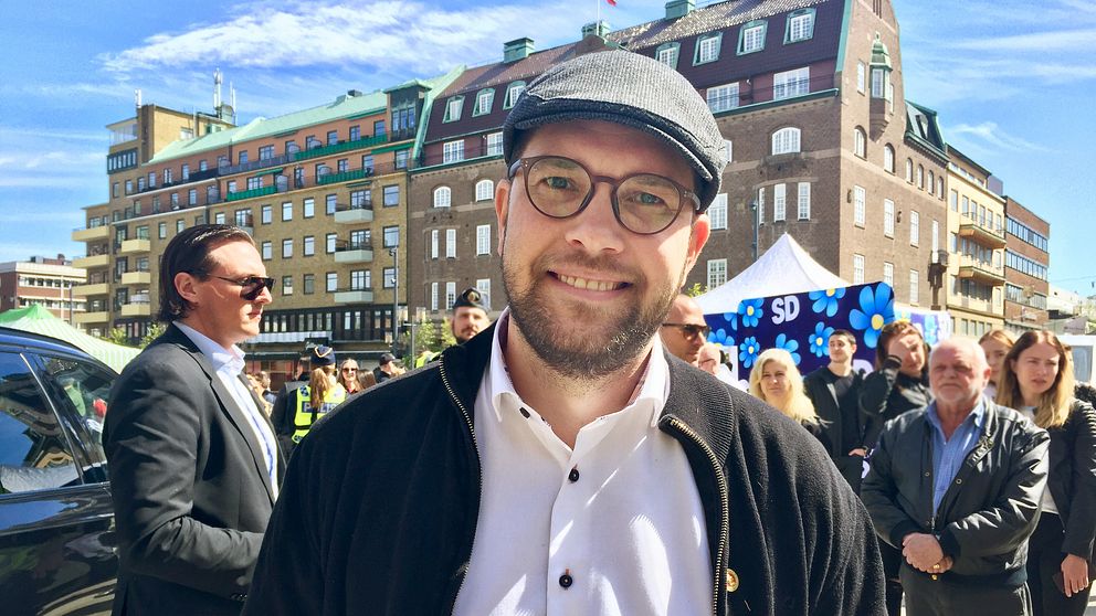 Jimmie Åkesson i keps och glasögon står på Fristadstorget i Eskilstuna. I bakgrunden skymtar EU-tält, lite åhörare, poliser och Säpo.