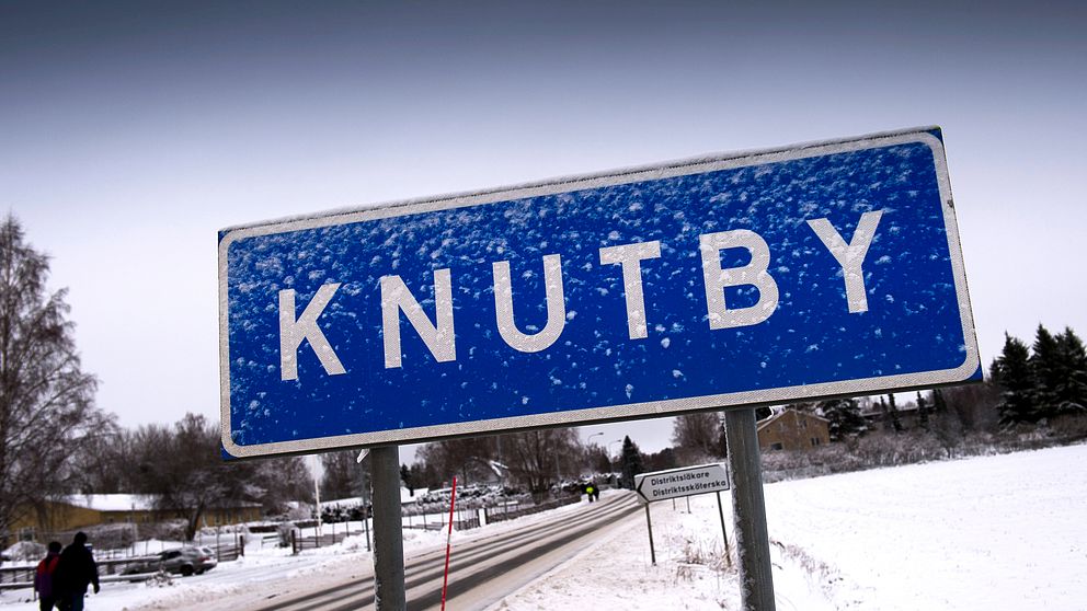 Vit och blå vägskylt som det står Knutby på. Delvis täckt av snö.
