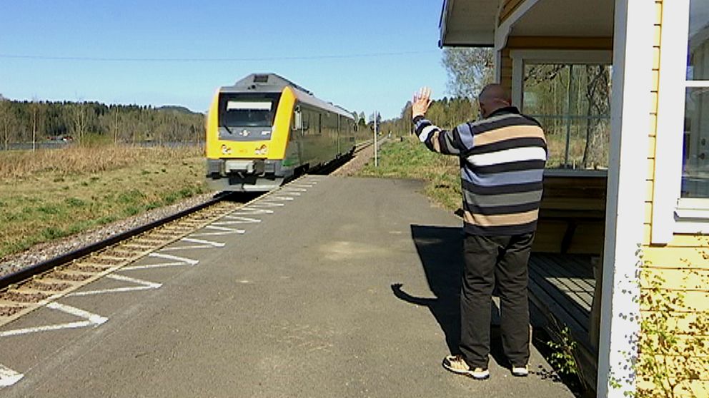 Äldre man vinkar åt ett förbipasserande tåg vid Oleby station.