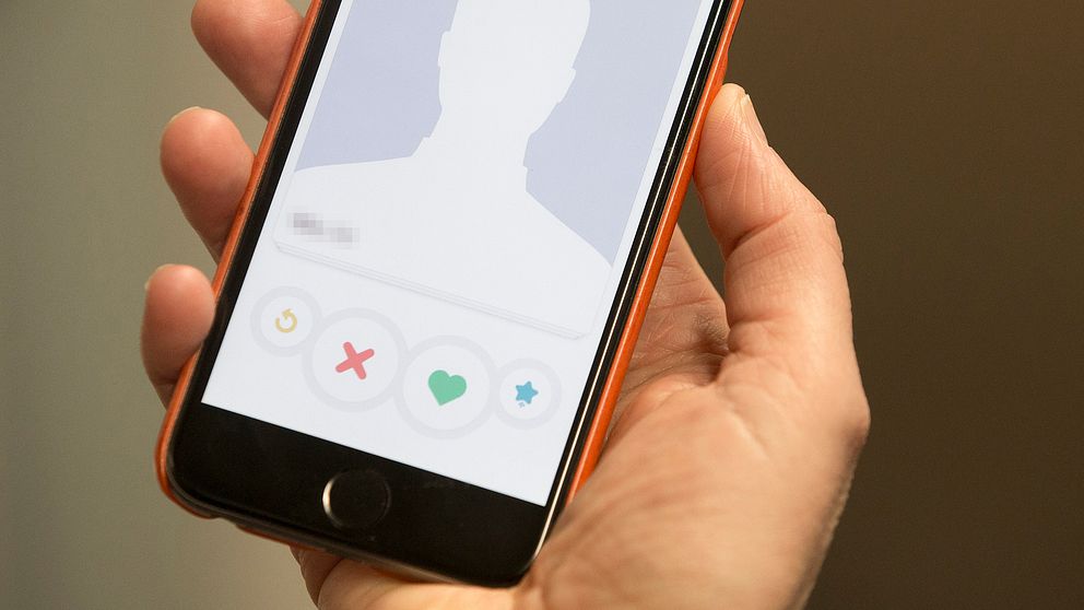 närbild på hand som håller mobil, på skärmen visas en anonym profilsida på en dejting-app