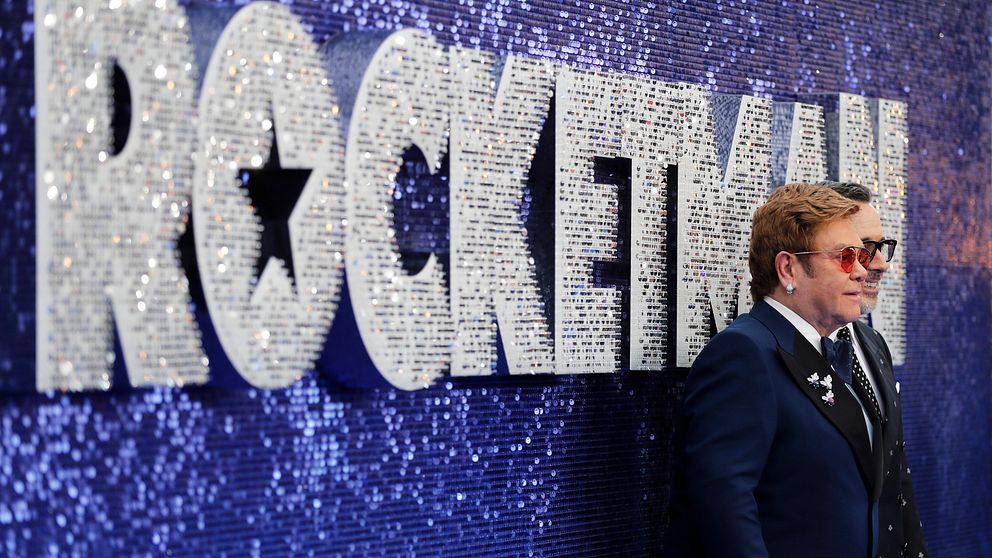 Elton John och producenten David Furnish poserar framför en Rocketman-skylt.