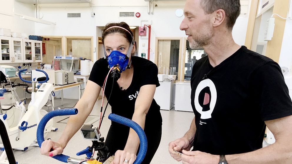 Malin Gotlin på en träningscykel. På sig har hon en andningsmask och en svart SVT-tröja.