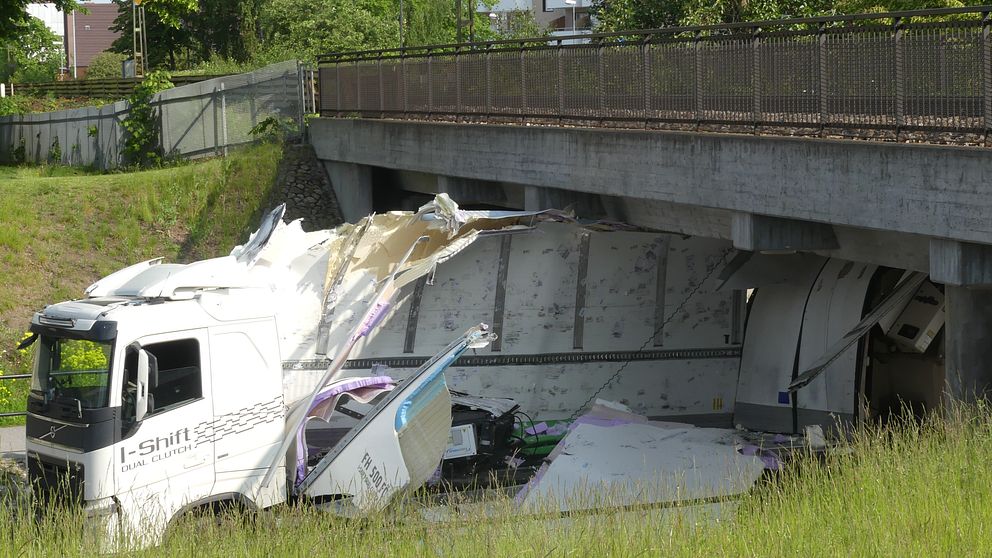 En lastbil sitter fast mitt under järnvägsbron. Sidorna på lastbilen har slagits sönder och ligger utfläkta över asfalten.