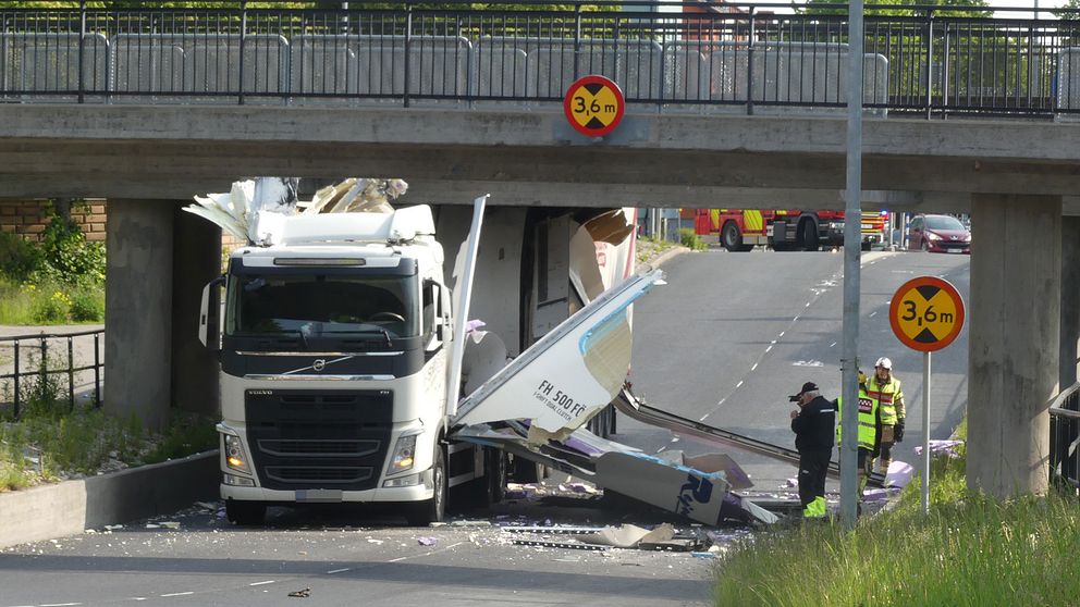 En lastbil sitter fast mitt under järnvägsbron. Sidorna på lastbilen har slagits sönder och ligger utfläkta över asfalten.