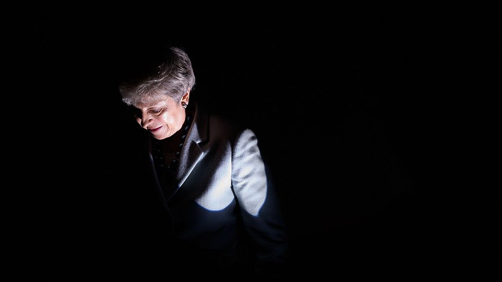 Theresa May står i ett mörkt rum.
