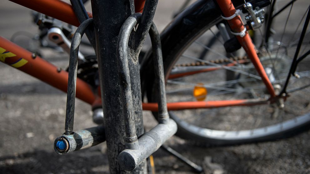 En cykel står parkerad i ett smutsigt cykelställ. Två cykellås hänger från cykelstället.