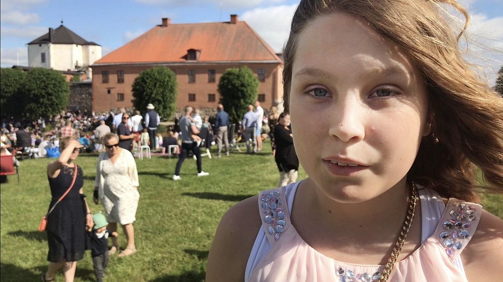 Eleven Emilia Ericson från Stenkullaskolan står på gräsmattan nedanför Nyköpingshus. I bakgrunden syns mängder med människor.
