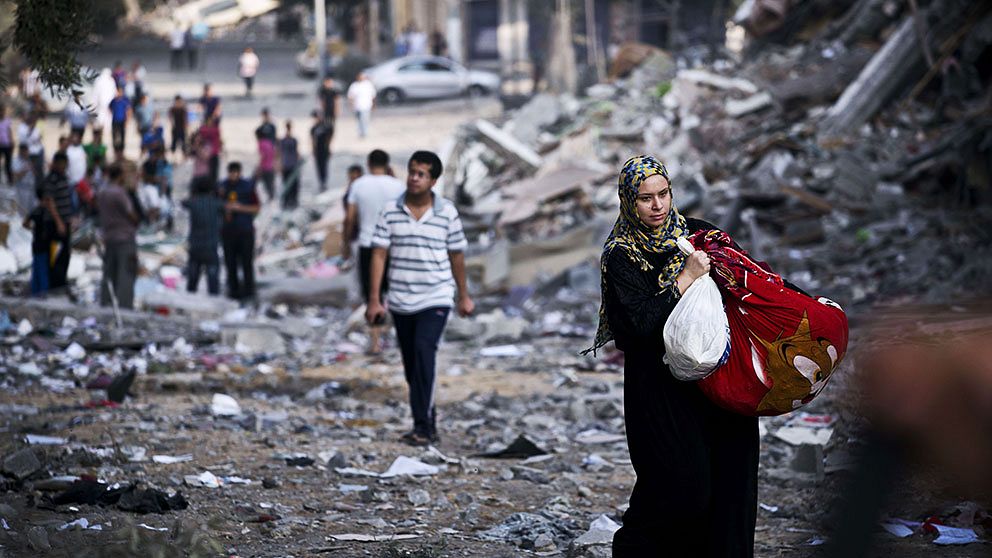 Kvinna bär sina ägodelar från sitt förstörda hem i Gaza City.