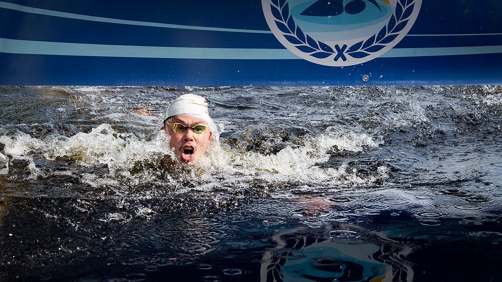 huvudet på en man i simglasögon och simmössa sticker upp ur vattnet där han simmar i mål