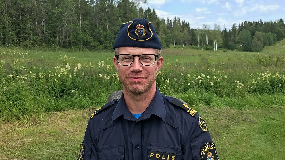 porträttbild på en man i polisuniform framför en äng med skog i bakgrunden