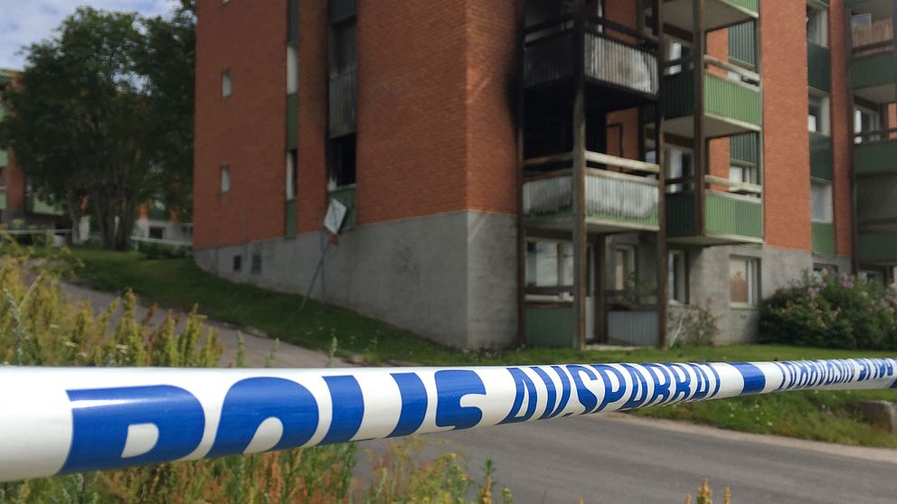 Polisens avspärrningsband i förgrunden. I bakgrunden syns ett brandskadat lägenhetshus.