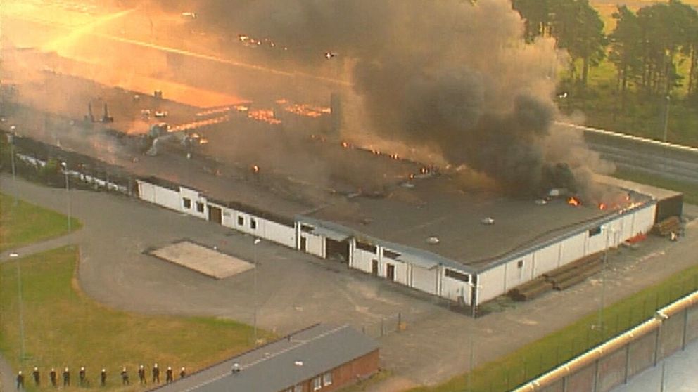 Flygbild över Tidaholmsanstalten i brand den 23 juli 1994, längst ner t v föser beväpnad polis in fångarna som gett upp