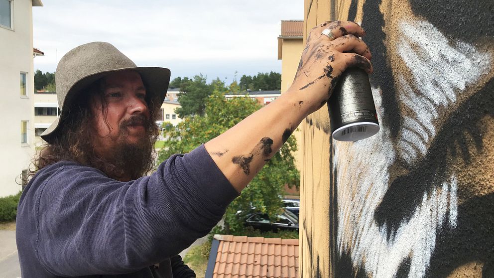 Charlie Granberg målar en husvägg med en sprejburk.