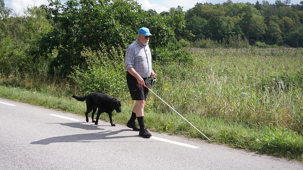Stellan Jacobsson går längs med en väg med sin ledarhund.